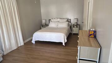 A bedroom with a bed, a ceiling fan, bedside lamps, a nightstand, and a wooden dresser.