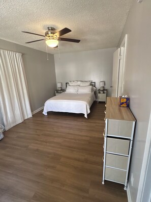 A bedroom with a bed, a ceiling fan, bedside lamps, a nightstand, and a wooden dresser. - Quaint 3-bedroom house with AC in welcoming Wichita (Wichita)