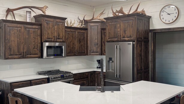A modern kitchen with dark wooden cabinets, stainless steel appliances, a large island with bar stools, and antler decorations.