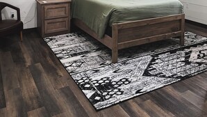 A bedroom with a wooden bed, a nightstand, a wall-mounted deer antler, a ceiling fan, and a patterned rug.