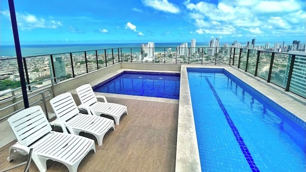 Una piscina en la azotea con sillones de descanso y vistas a la ciudad.