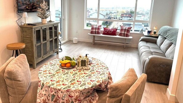 Una sala de estar con una mesa de comedor, sofá y un ventanal con vistas a casas.