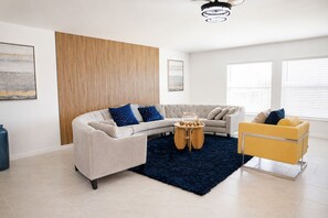 A modern living room with a curved sofa, a round coffee table, and a yellow armchair. - Casa Solana (North Fort Myers)