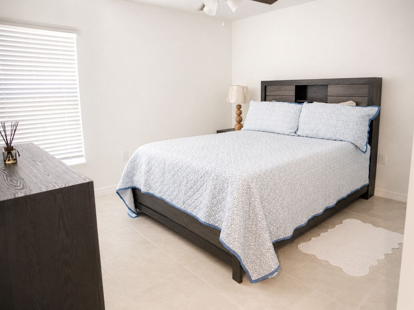 A bedroom with a bed, bedside table, lamp, and a small rug.