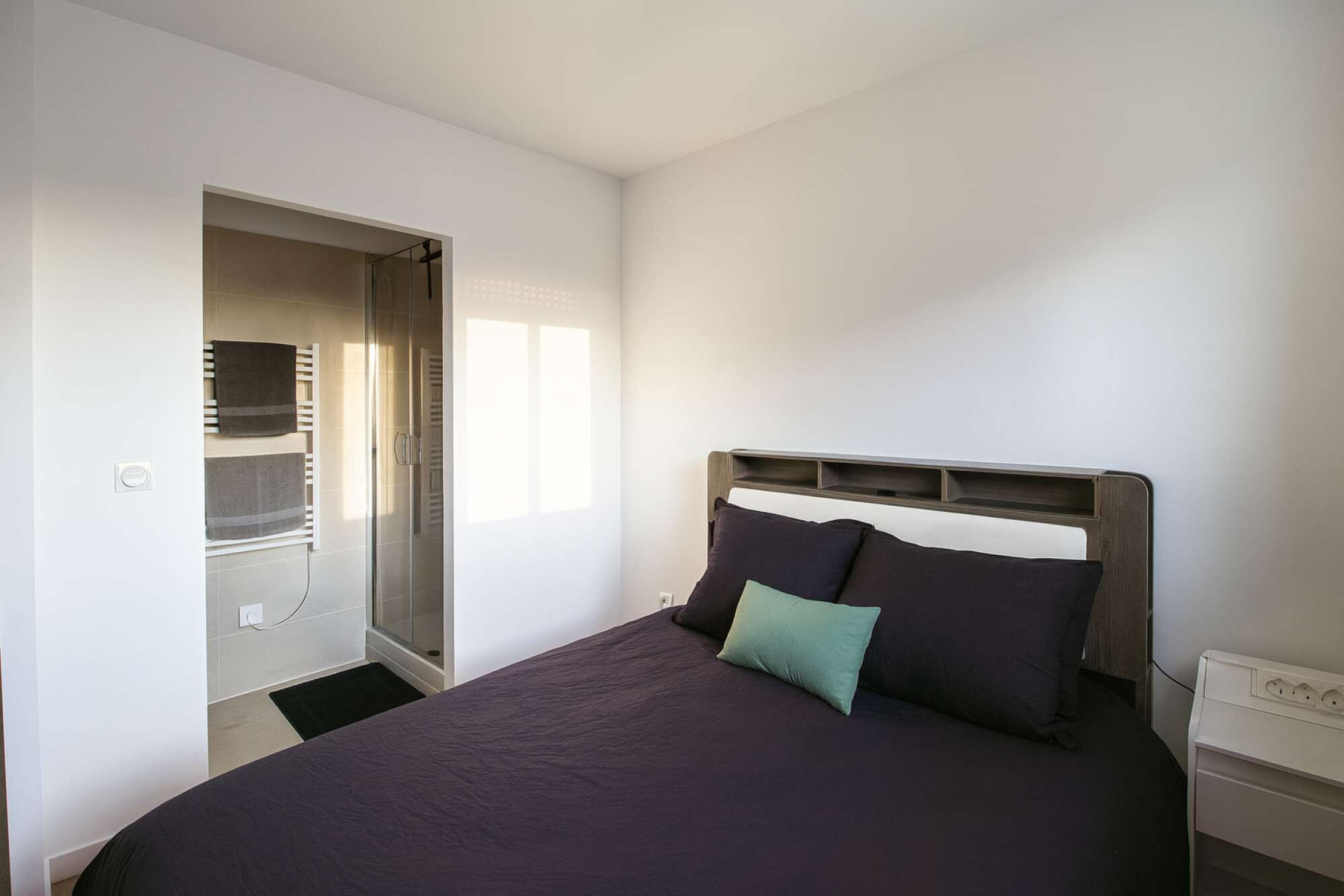 Un dormitorio con cama, mesita de noche, armario empotrado con espejo y perchero.
