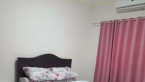Un dormitorio con una cama, una mesita de noche, una alfombra y un ventanal con cortinas rosas.