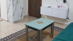 Una sala de estar con un mueble de estilo mármol, un televisor montado en la pared, una mesita con un juego de mesa y un sofá verde.