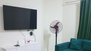 Una sala de estar con un televisor de pantalla plana, un ventilador de pie, un sofá color turquesa y una mesa de centro.