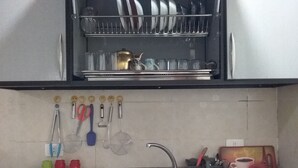 Una cocina con un lavamanos de acero inoxidable, un escurreplatos arriba y varios utensilios colgados en la pared.