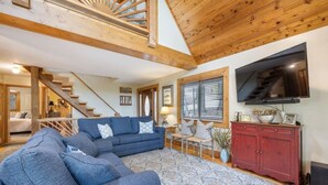 A spacious living room with a blue sectional sofa, a red cabinet, and a large TV. - Water's Edge - Lakeside retreat (Winchester)