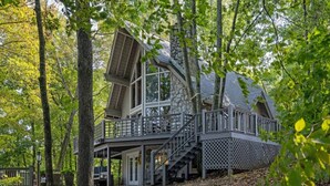 A multi-level stone cabin with a balcony, surrounded by trees. - Water's Edge - Lakeside retreat (Winchester)