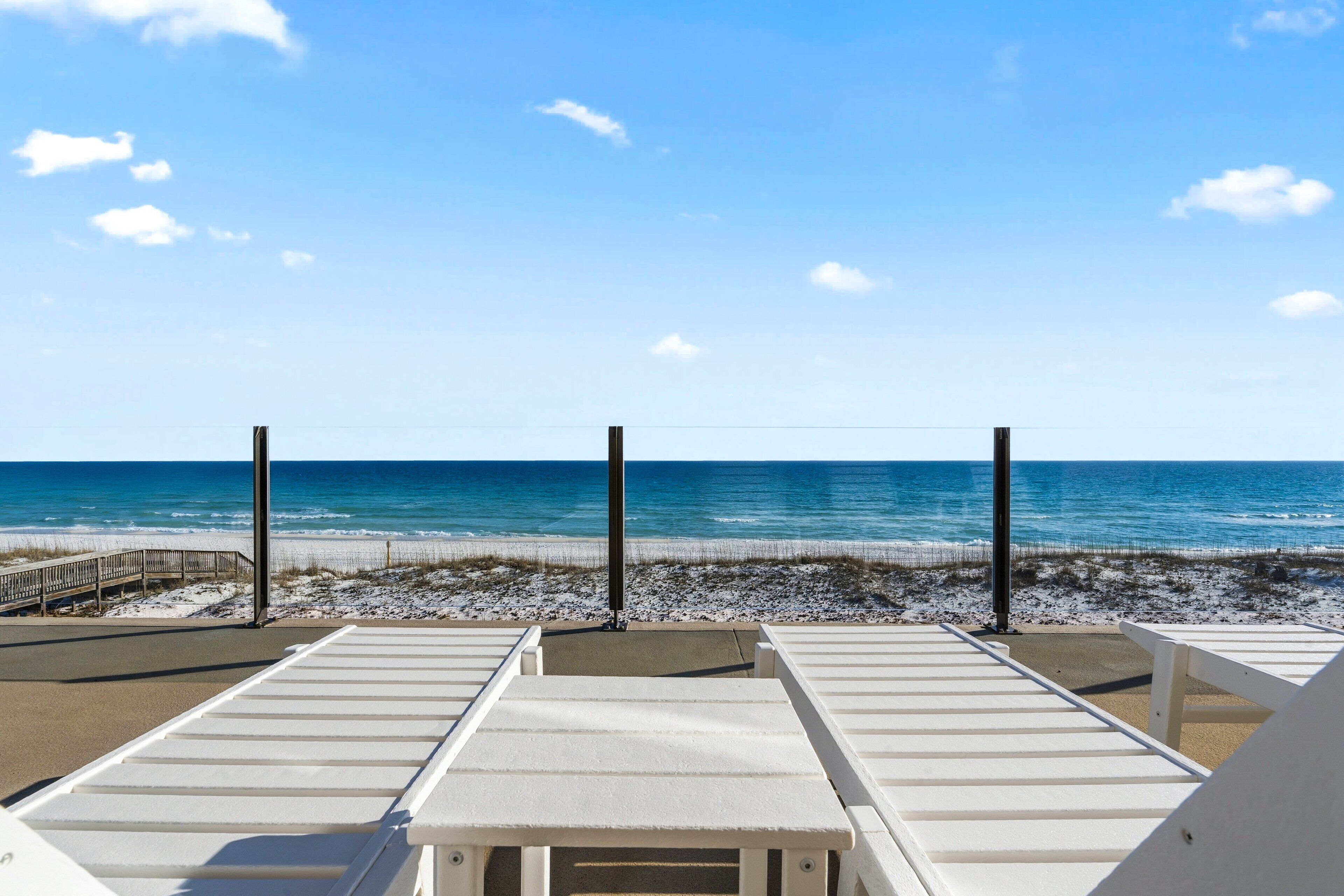 A beach view with white lounge chairs and a wooden walkway leading to the shore.