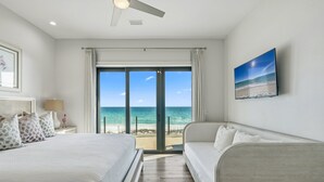Ein Schlafzimmer mit einem großen Bett, einer Couch, einem Deckenventilator, einem Nachttisch, einer Lampe und einem Bild von einer Strandansicht.