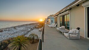 Ein Balkon mit weißen Liegestühlen und Blick auf den Strand bei Sonnenuntergang.