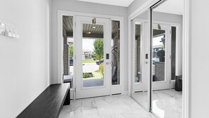 Un hall d’entrée moderne avec un banc, une porte vitrée donnant sur un patio et un intérieur de couleur blanche.