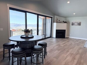 A modern living room with a large window offering a mountain view, a fireplace, and a round dining table with stools.