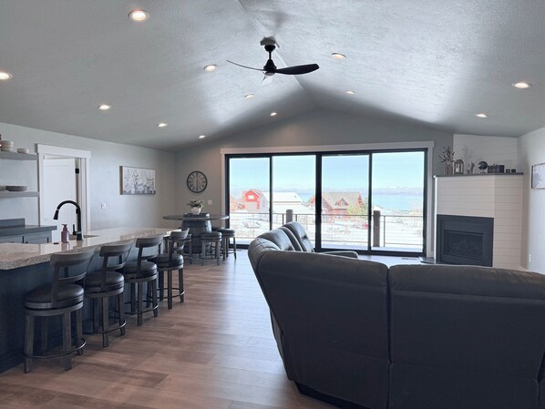 A spacious kitchen with a central island, bar stools, and a large window offering a view of a red house and mountains.