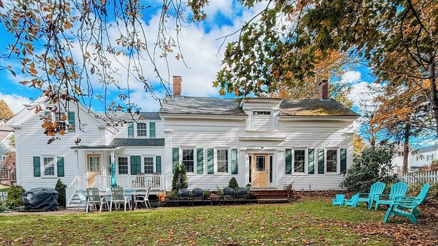 A two-story white house with a front porch, green shutters, and a covered patio area with chairs. - Charming Historic home steps away from downtown (Bath)