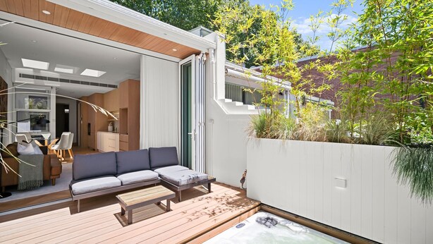 Un espacio exterior moderno con terraza de madera, sofá y jacuzzi.