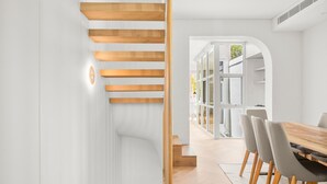 Un interior moderno con una escalera de madera, un comedor con una mesa y sillas de madera, y una vista a través de un arco hacia otra habitación.