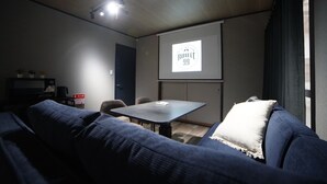 A modern living room with a dark blue sofa, a small table, and a projector screen displaying a logo. - Route 99 Miyagino (Hakone)