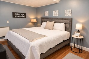 A bedroom with a bed, bedside lamps, a wall-mounted sign, and decorative wall art. - Overlook Condo 21-C Studio ~ Off Mountain ~ 6 miles to Snowshoe Mountaintop Village (Slatyfork)