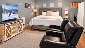 Une chambre à coucher avec un lit, un téléviseur posé sur un meuble en bois, un canapé en cuir noir et un meuble en bois avec des tiroirs.