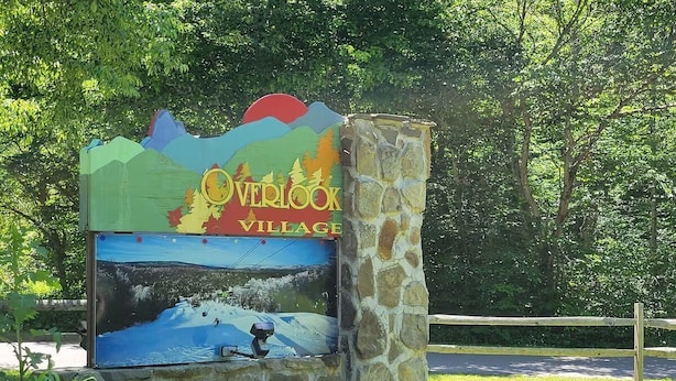 Un panneau indiquant l’entrée de Overlook Village, agrémenté d’une illustration représentant un paysage pittoresque.