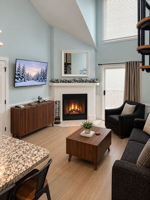 A living room with a fireplace, a television, a sofa, and a dining area. - Whistlepunk #43: 1 bedroom with Loft, Slopeside (Snowshoe)
