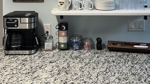 Et køkken med hylder, der indeholder gryder, tallerkener, kopper og en kaffemaskine.