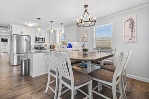 A modern kitchen with white cabinetry, stainless steel appliances, and a dining area with a wooden table and white chairs.