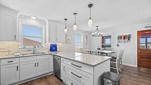A modern kitchen with white cabinetry, a granite countertop, and pendant lighting. - Beach Scout | 500 ft to the beach | Hot Tub (Kitty Hawk)