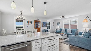 A modern kitchen with a central island, white cabinetry, and a stainless steel dishwasher. - Beach Scout | 500 ft to the beach | Hot Tub (Kitty Hawk)