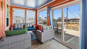 A covered deck with wicker furniture and a view of the ocean. - Beach Scout | 500 ft to the beach | Hot Tub (Kitty Hawk)