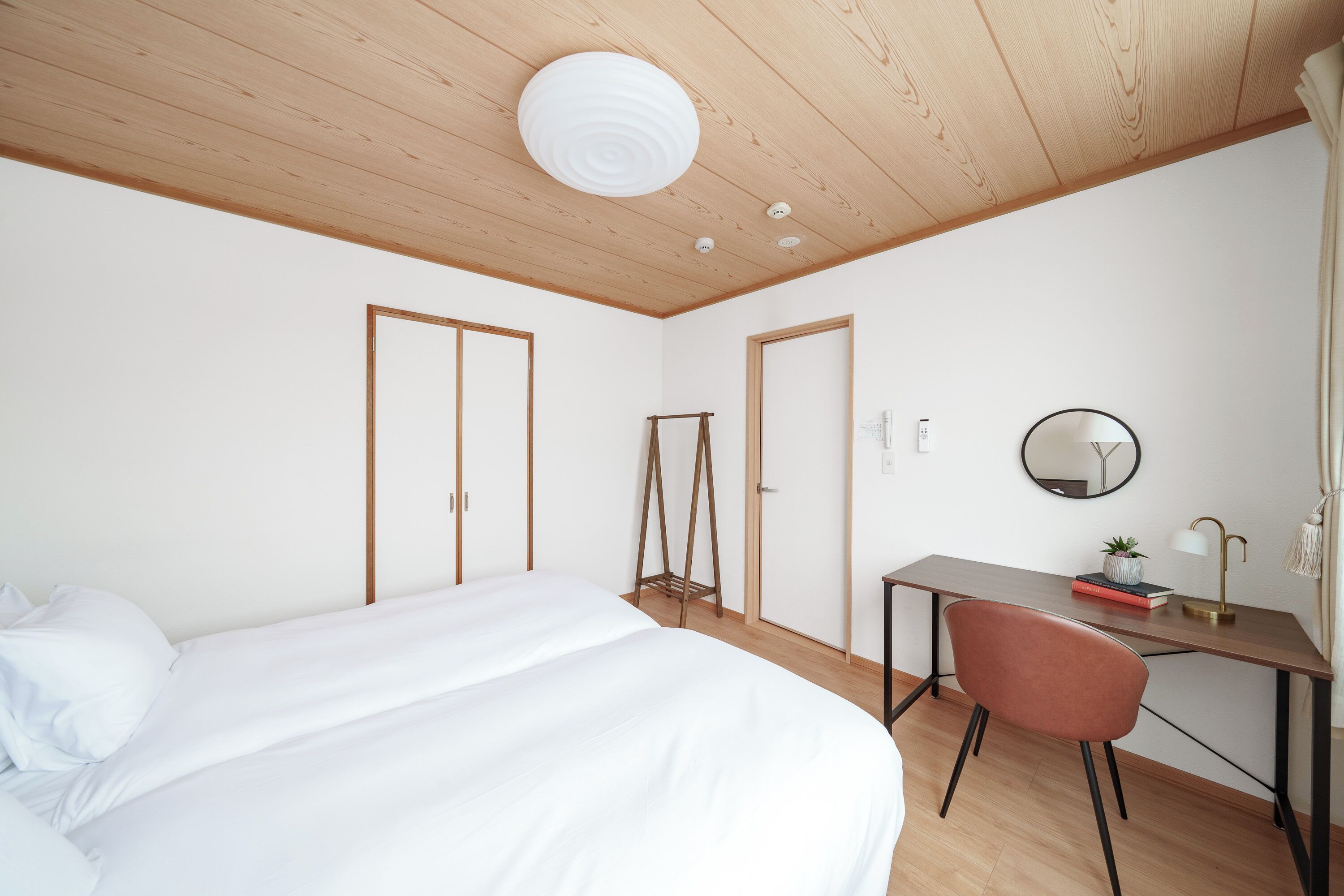 A bedroom with a bed, a desk, a chair, and a mirror.