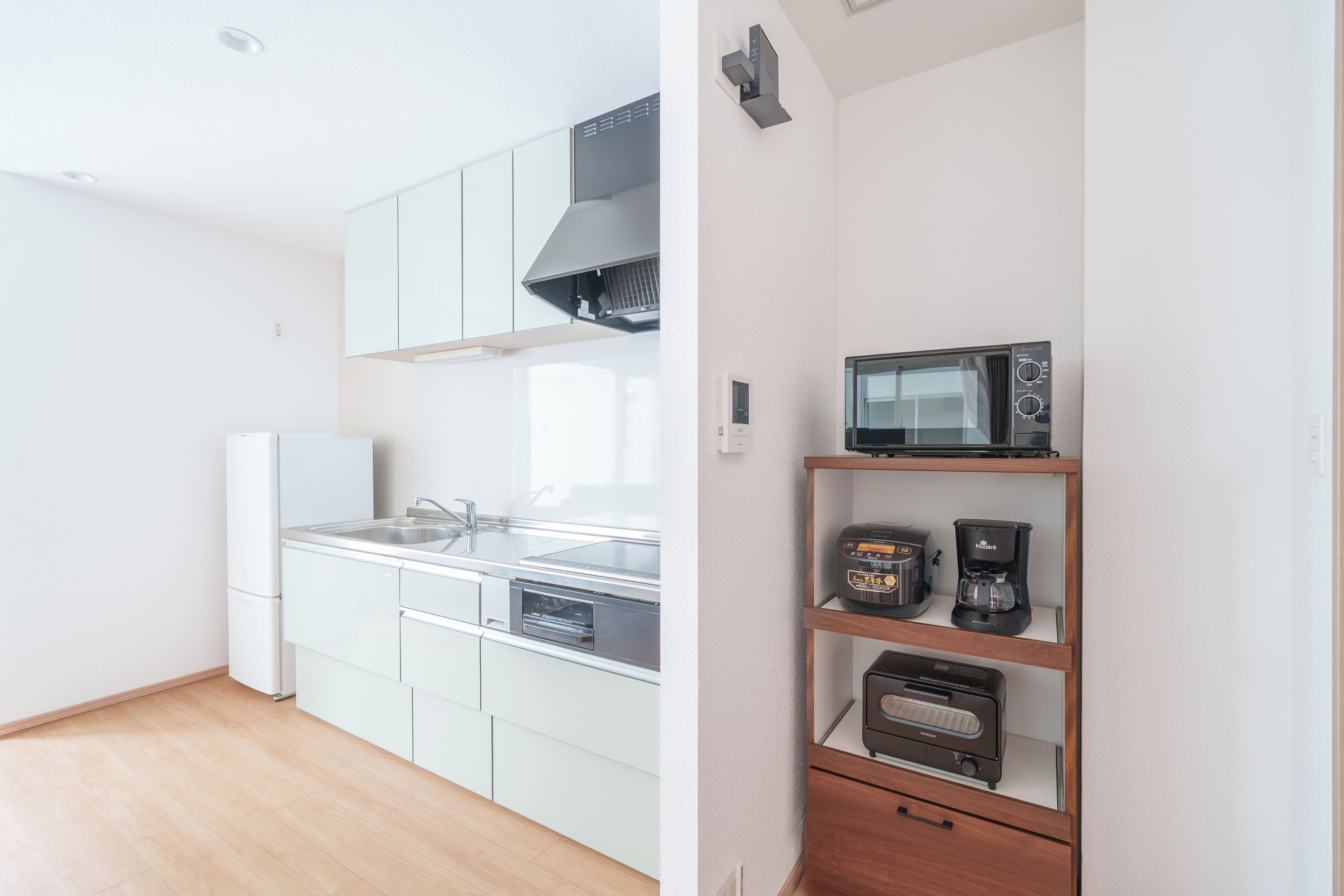 A modern kitchen with white cabinets, a stainless steel sink, a built-in oven, and a microwave on a wooden shelf.