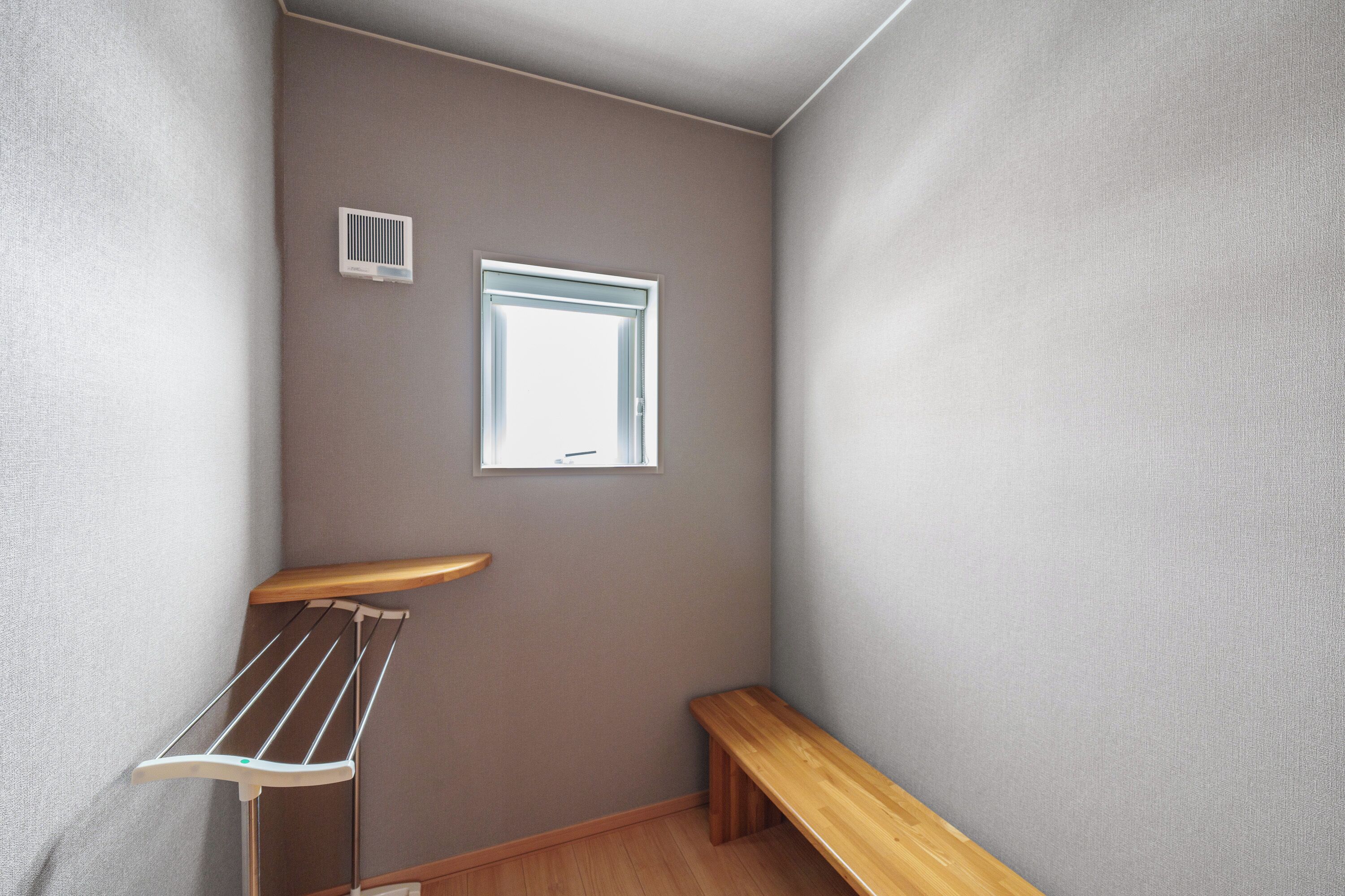 A corner room with a wooden bench, a wall-mounted drying rack, and a window.