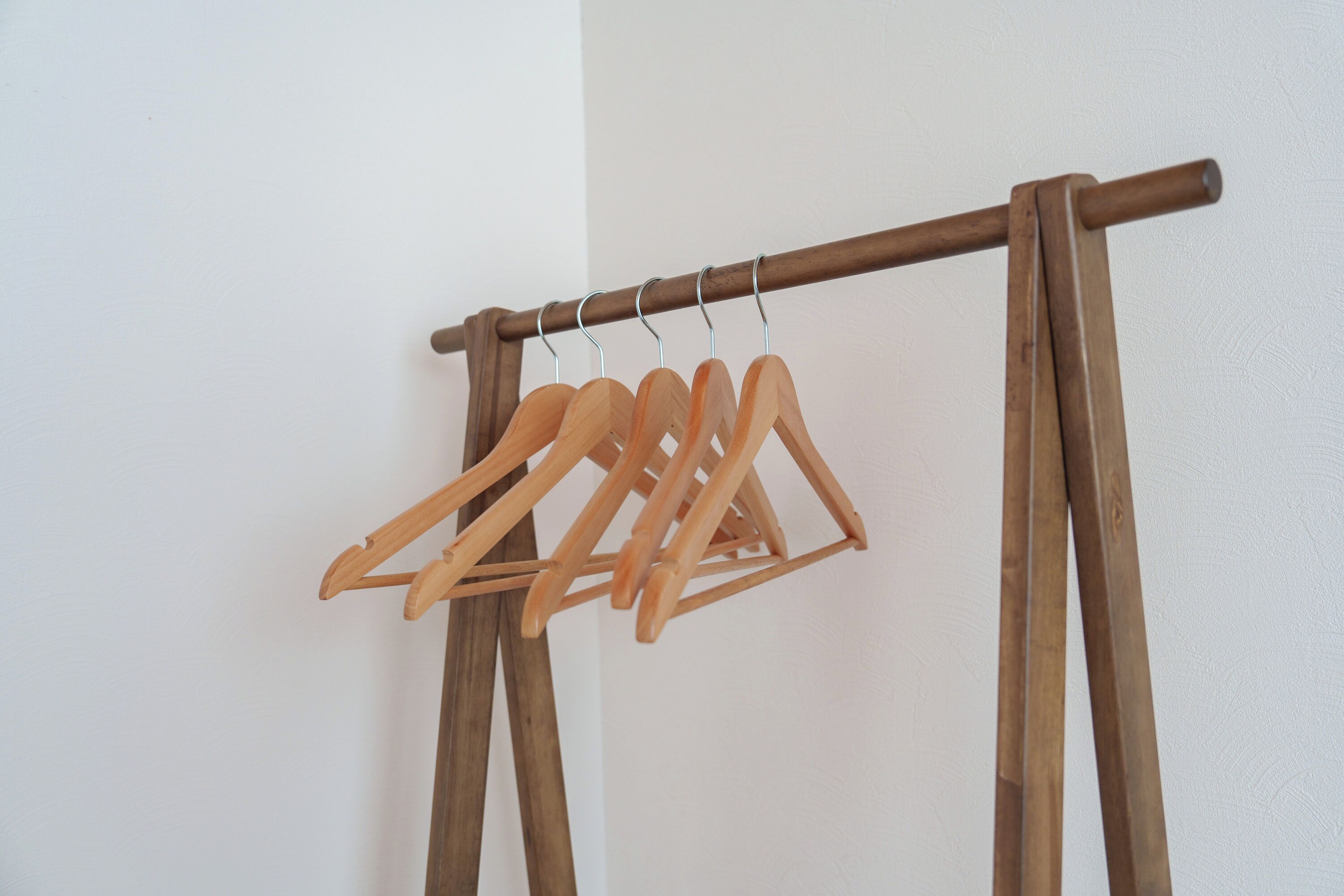 A wooden clothes rack with several wooden hangers against a plain wall.