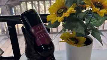 Una botella de vino, dos copas y un girasol en maceta sobre una mesa junto a una ventana.