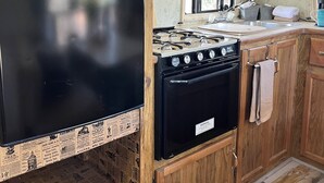 Een kleine keuken met een zwarte koelkast, een magnetron, een fornuis en houten kastjes.