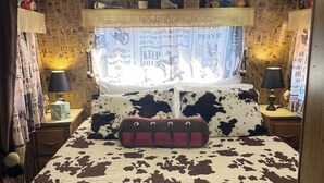 Een slaapkamer met een roodbruine sprei met koeienprint, een raam met uitzicht op de lucht en een muur met kranten behang.