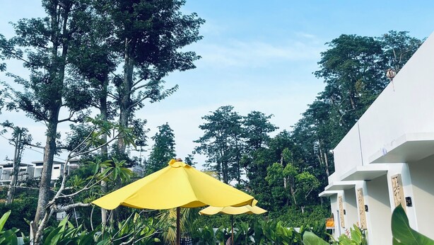 A courtyard with a yellow umbrella, wooden furniture, and lush greenery. - Satria Bali Homestay (Pecatu)