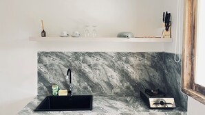 A kitchen with a black sink, marble backsplash, and a shelf above holding kitchenware and a knife set. - Satria Bali Homestay (Pecatu)