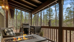 Eine überdachte Terrasse im Freien mit Feuerstelle, Grillmöglichkeit und Sitzgelegenheiten.
