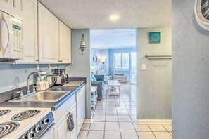 A kitchen with a stove, sink, and coffee maker. There is a living room with a couch and a coffee table. - Bluewater 821 (Myrtle Beach)