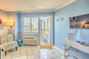 A room with a blue wall, a white air conditioner, a chair, a television, and a door leading outside. - Bluewater 821 (Myrtle Beach)