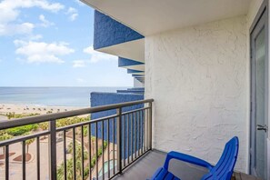 A balcony with a view of the beach and ocean, a blue chair, and a white textured wall. - Bluewater 821 (Myrtle Beach)