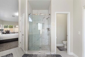 Une salle de bain moderne avec une douche à parois de verre, des toilettes et un lit dans la pièce adjacente.