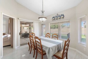 Un coin repas avec une table dressée pour quatre personnes, des chaises en bois, un lustre et une vue par les fenêtres.
