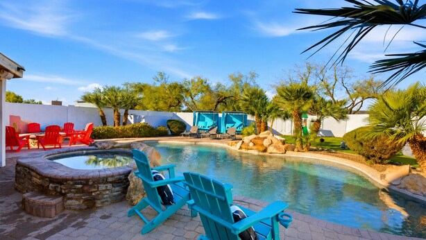 Una piscina con idromassaggio, circondata da poltrone Adirondack rosse e blu, palme e un muro in pietra.
